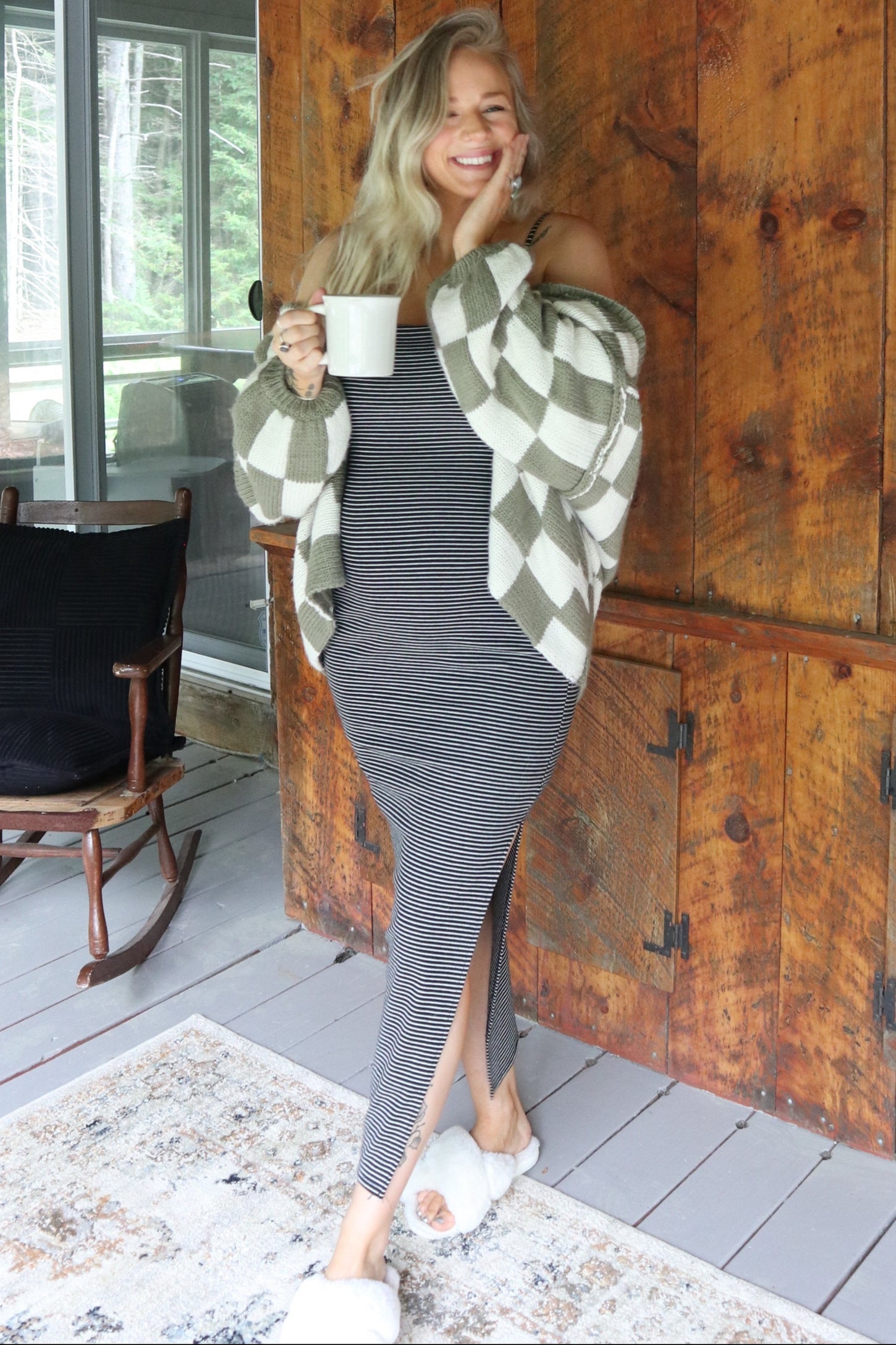 woman wearing a gray striped maxi dress with a thigh-high slit, layered with a cream and olive green checkered cardigan