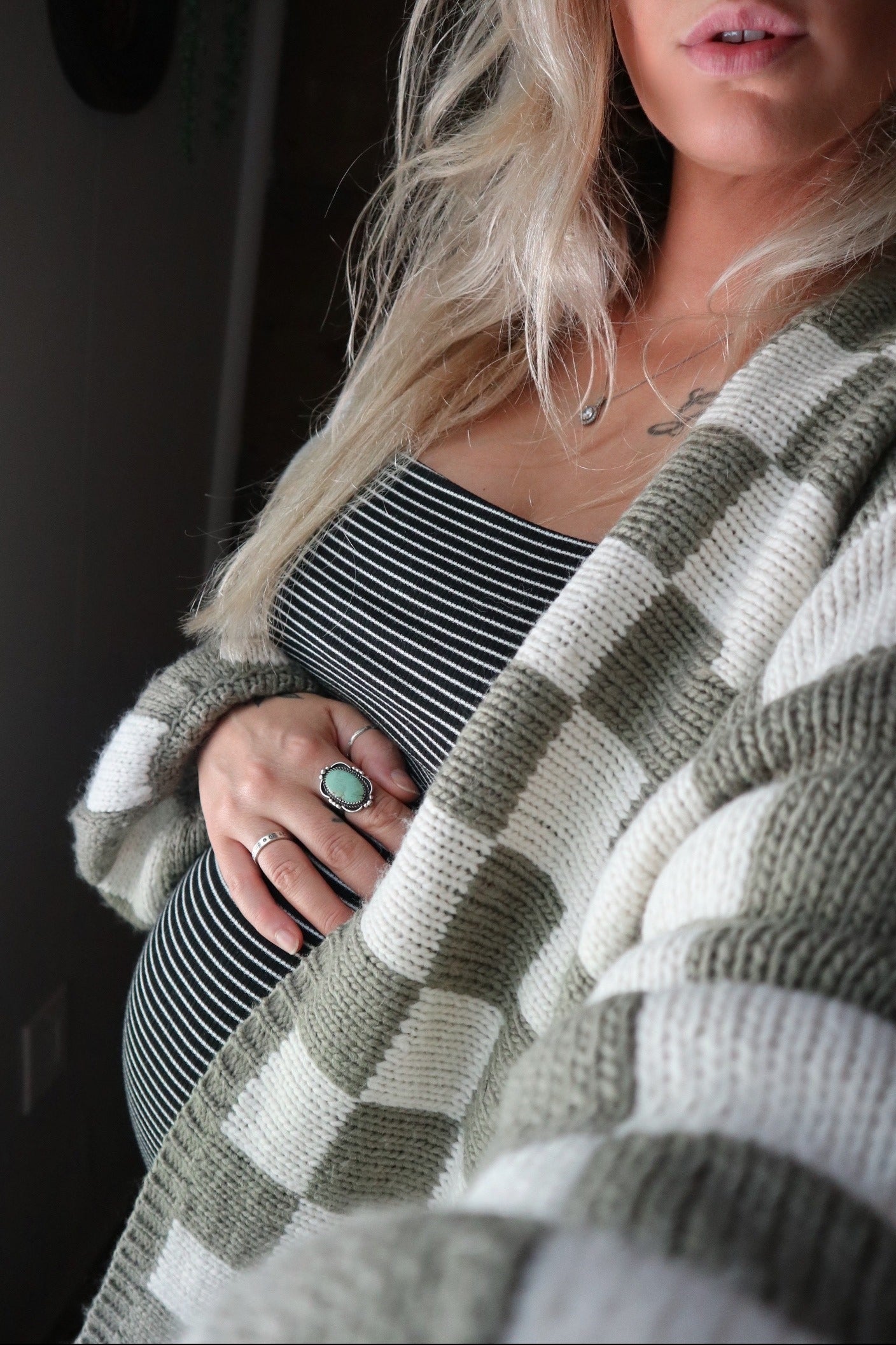 woman wearing a striped maternity dress and a green and white cardigan, holding her baby bump