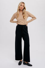woman wearing tan long sleeve crewneck top and black wide leg knit trousers with loafers