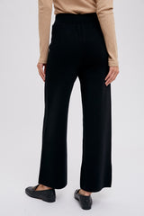 Rear view of woman wearing black wide leg knit trousers and tan long sleeve top with black loafers