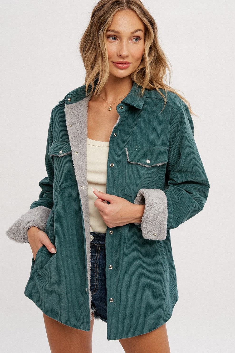 woman wearing a teal corduroy jacket with grey faux fur lining, button closures, and side pockets, styled with a tank top and shorts