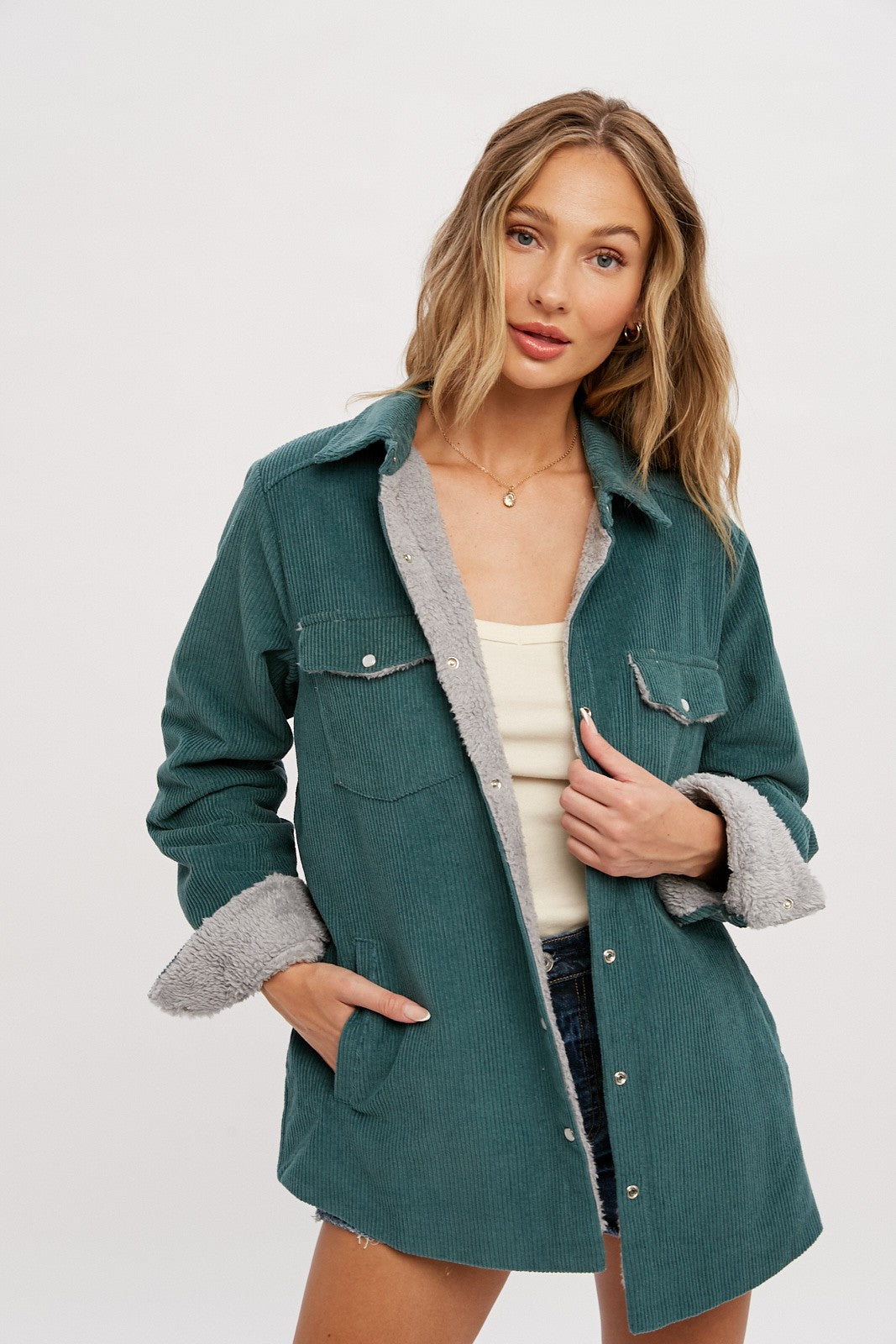 woman wearing a teal corduroy jacket with gray faux fur lining and pockets, styled with a tank top and denim shorts