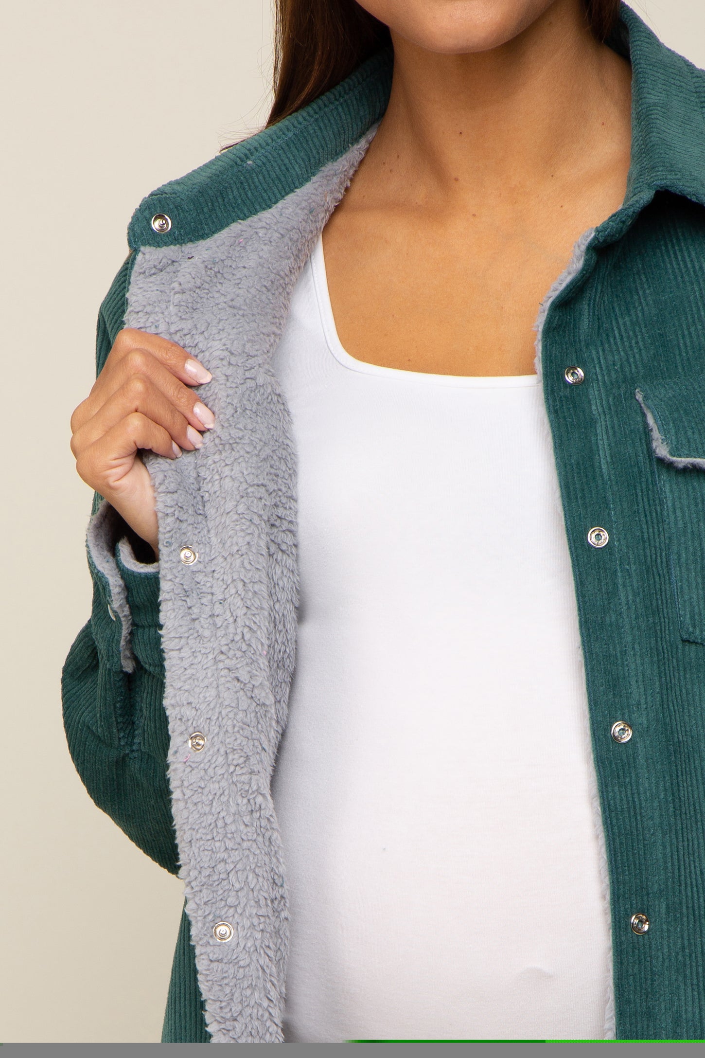 woman wearing a teal corduroy maternity jacket with a grey fleece lining and a white maternity top underneath, showing her baby bump