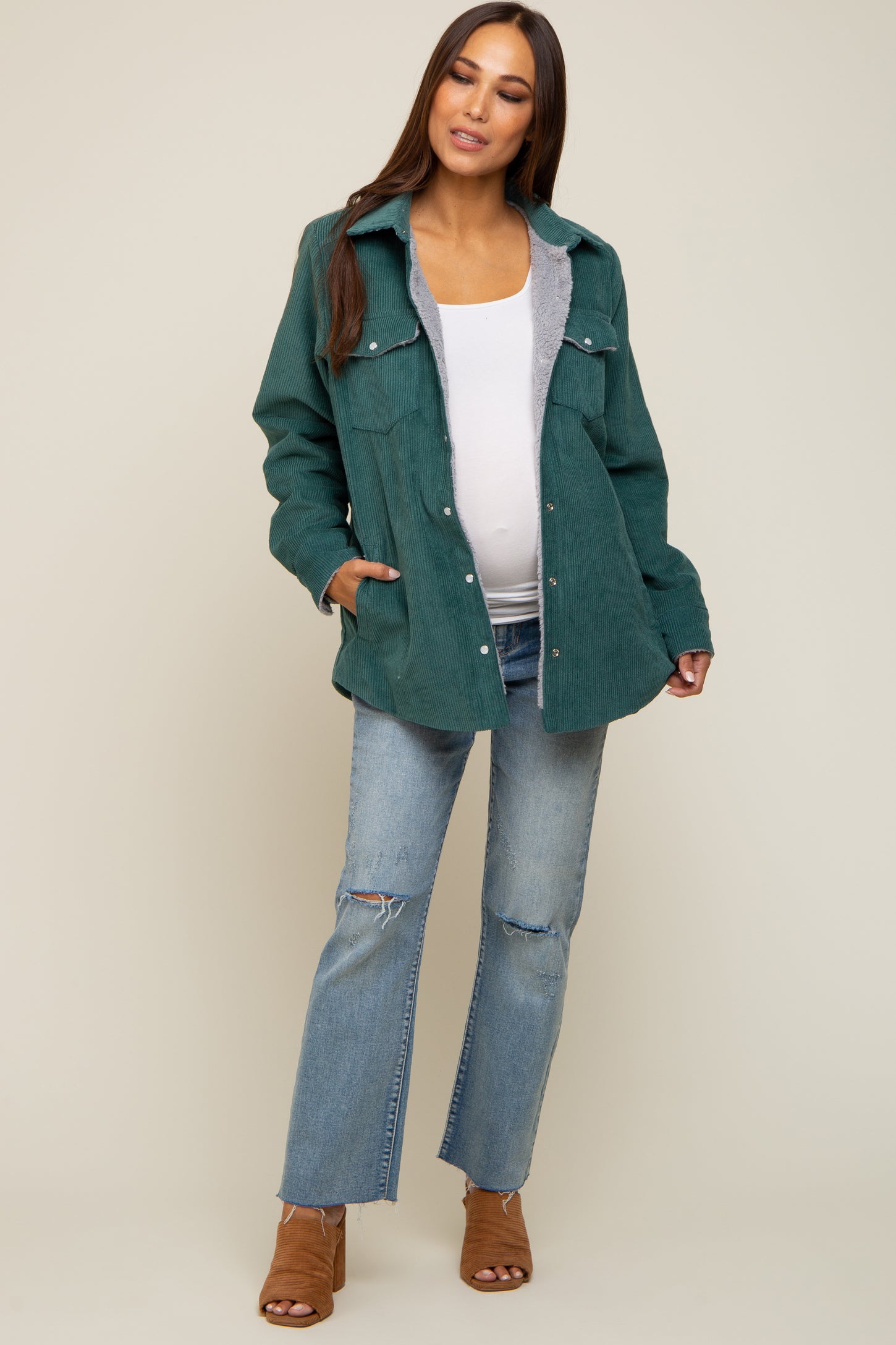 woman wearing a green corduroy maternity jacket over a white top and blue distressed jeans, showcasing her baby bump
