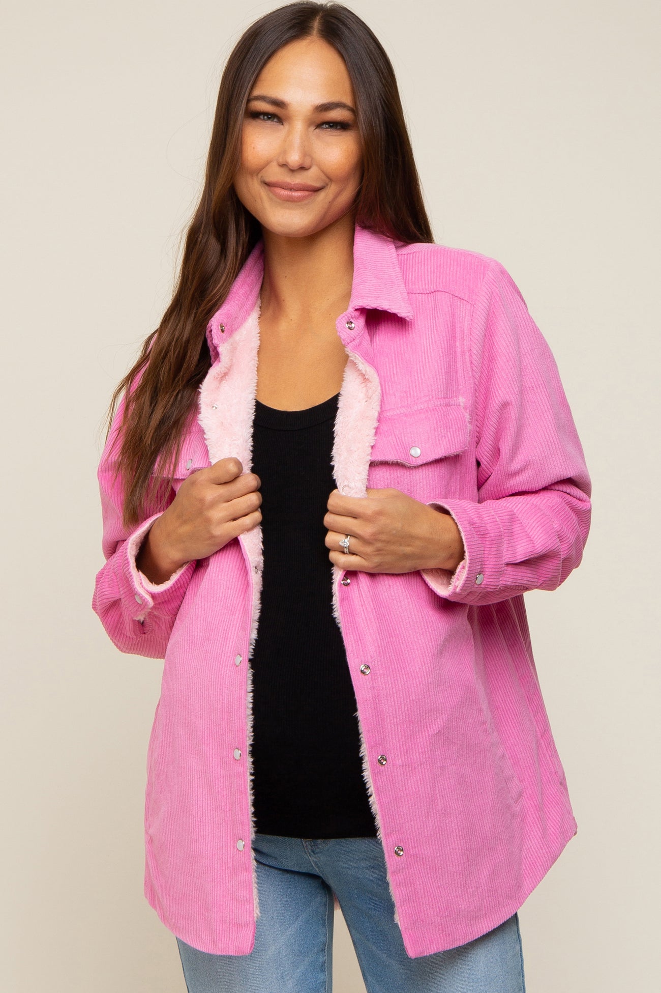 woman wearing a pink corduroy jacket with faux fur lining over a black top and blue jeans