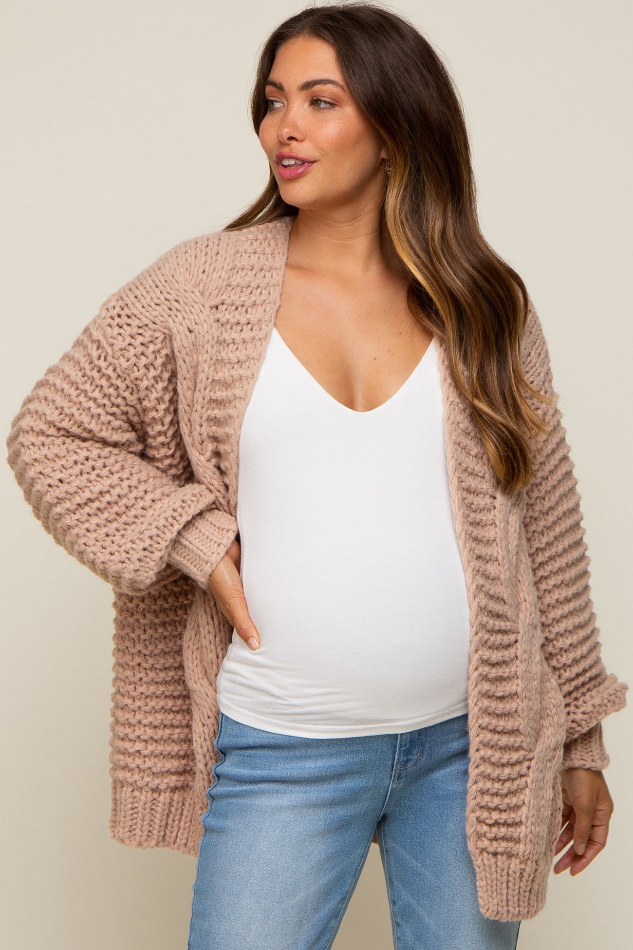Pregnant woman wearing a mauve chunky knit cardigan over a white maternity tank top and blue jeans