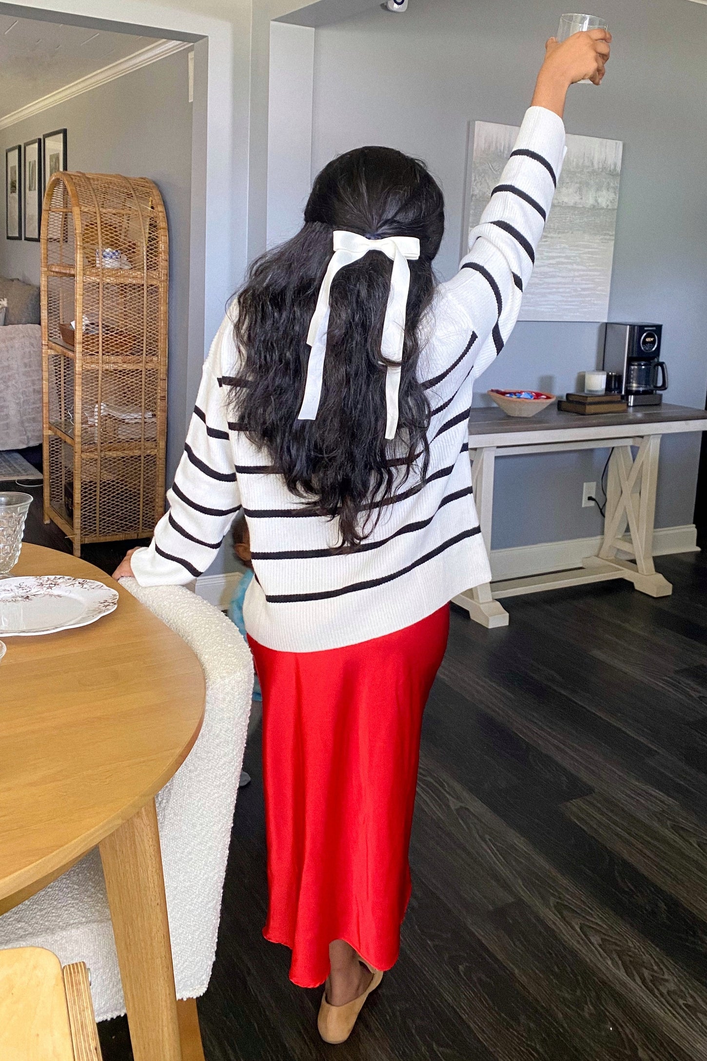 woman wearing a white striped sweater and a red satin midi skirt, holding a drink with one hand