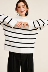 woman wearing a white and black striped oversized sweater with wide sleeves and high neckline