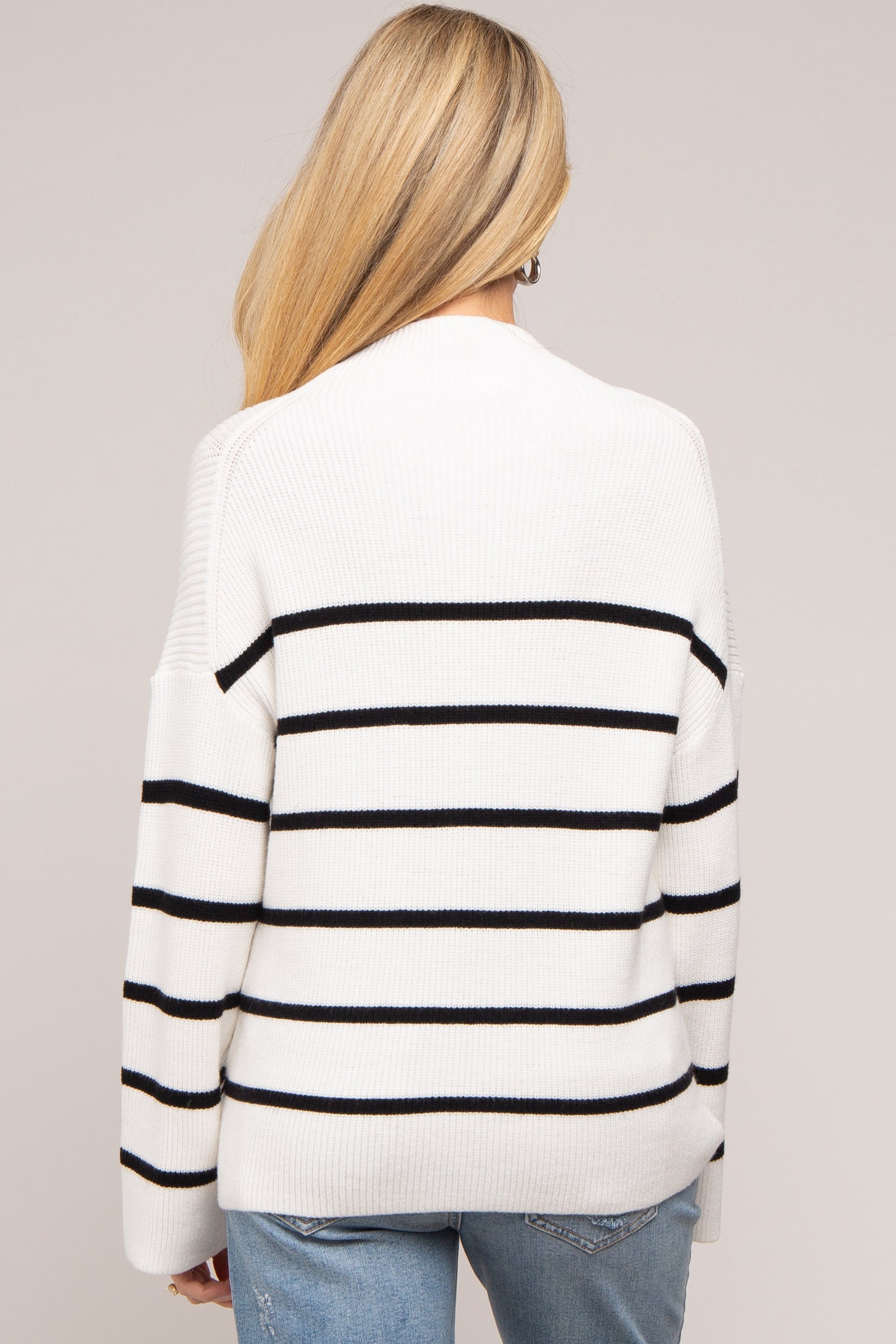 woman wearing a white and black striped maternity sweater, seen from the back, styled with relaxed fit and long sleeves