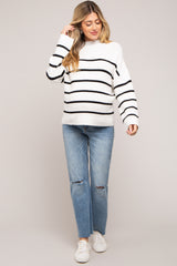 woman wearing a striped black and white maternity sweater with a relaxed fit and paired with light blue distressed jeans