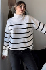 woman wearing a white and black striped sweater with a high neckline and long sleeves, posing in a casual setting