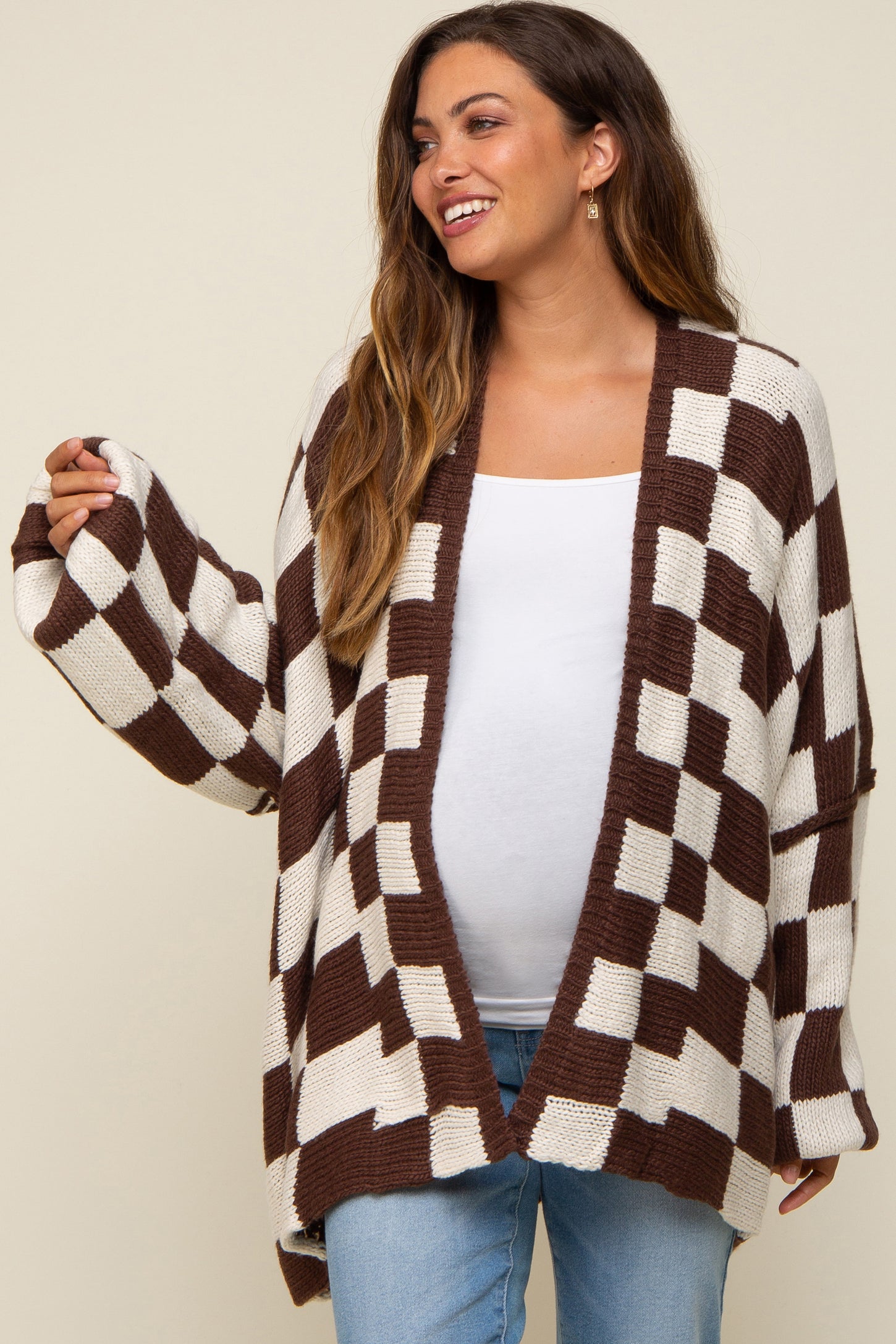 woman wearing a brown and white checkered maternity cardigan with a visible baby bump, paired with a white top and jeans