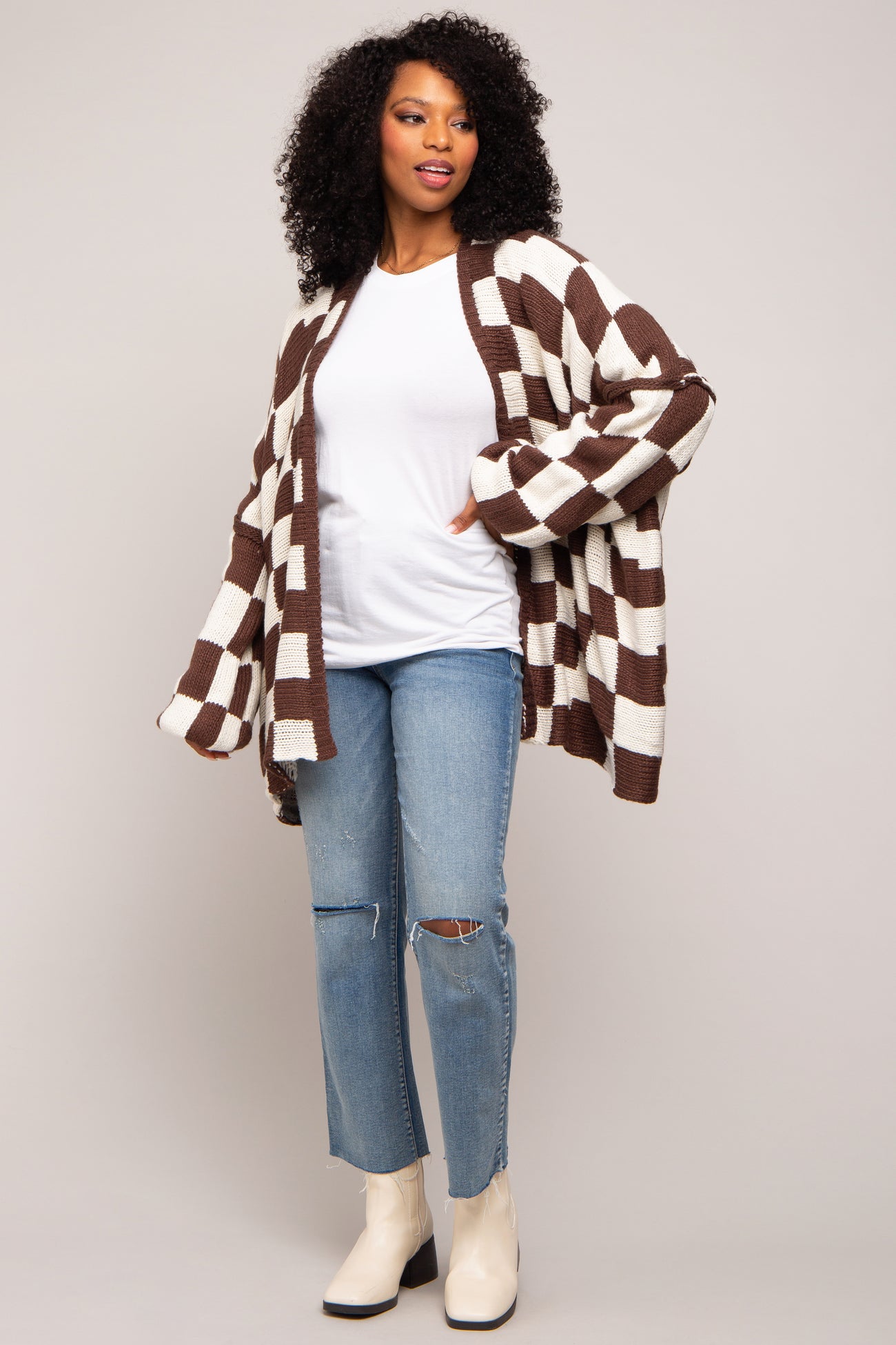 woman wearing a brown and cream striped oversized cardigan, white t-shirt, and ripped light blue jeans with ankle boots