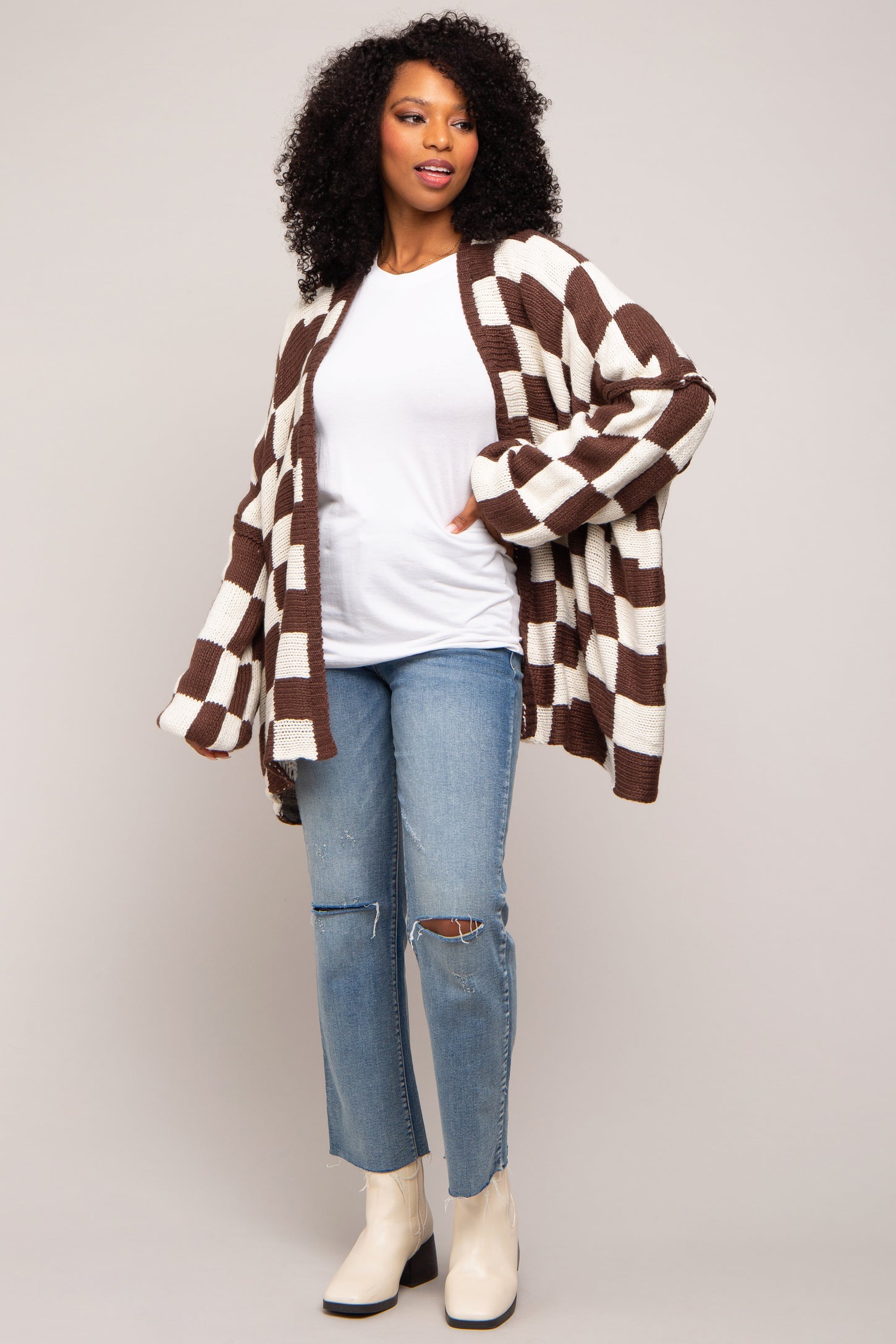 woman wearing a brown and cream striped oversized cardigan, white t-shirt, and ripped light blue jeans with ankle boots
