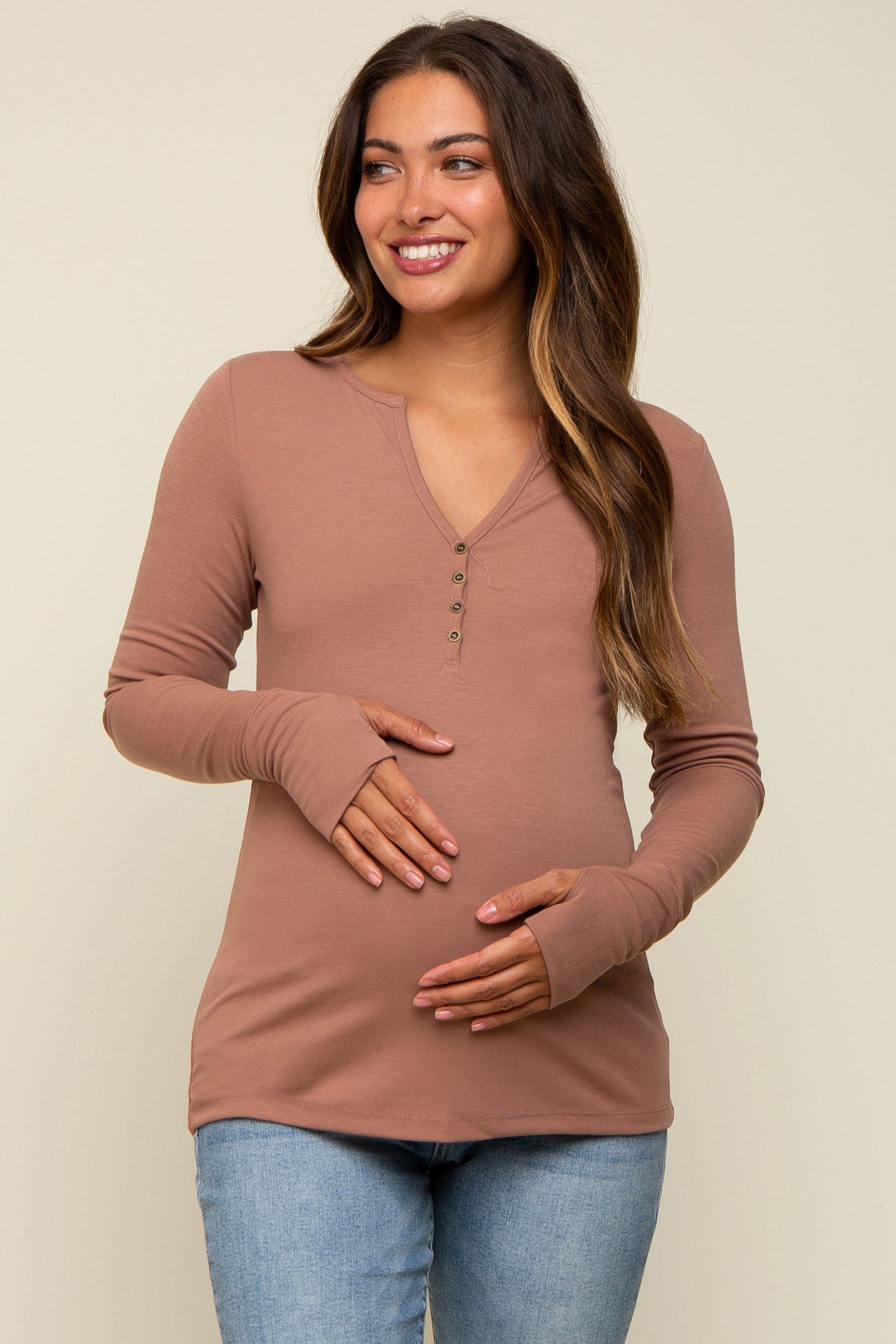 woman wearing a dusty rose long sleeve maternity top with buttons and holding her baby bump