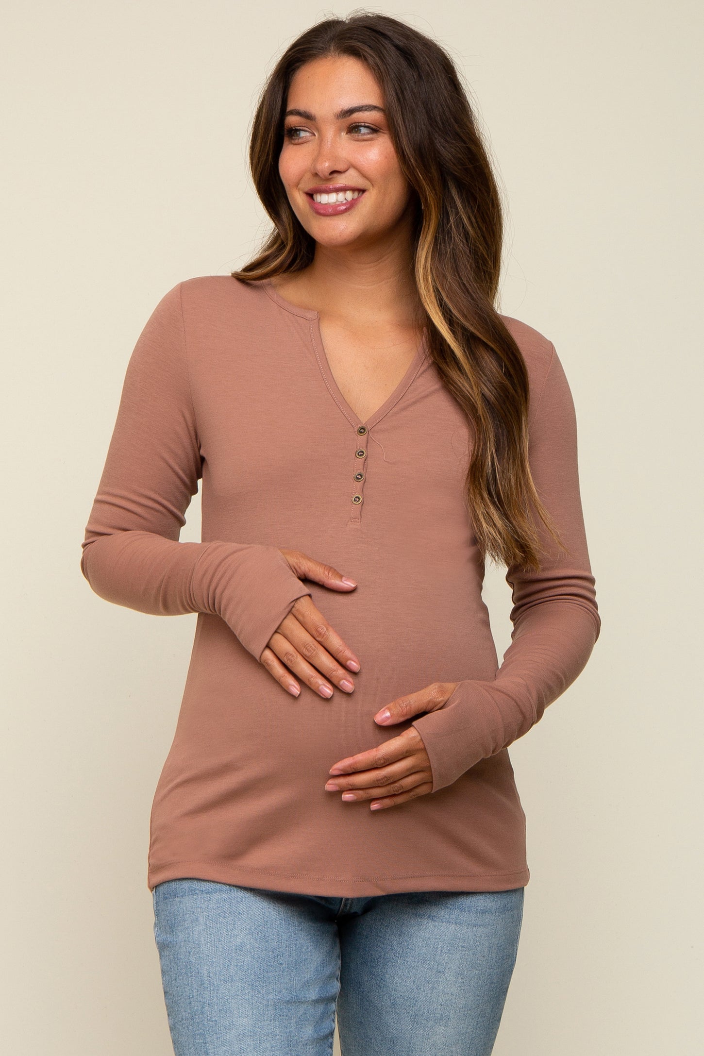 woman wearing a dusty rose long sleeve maternity top with buttons and holding her baby bump