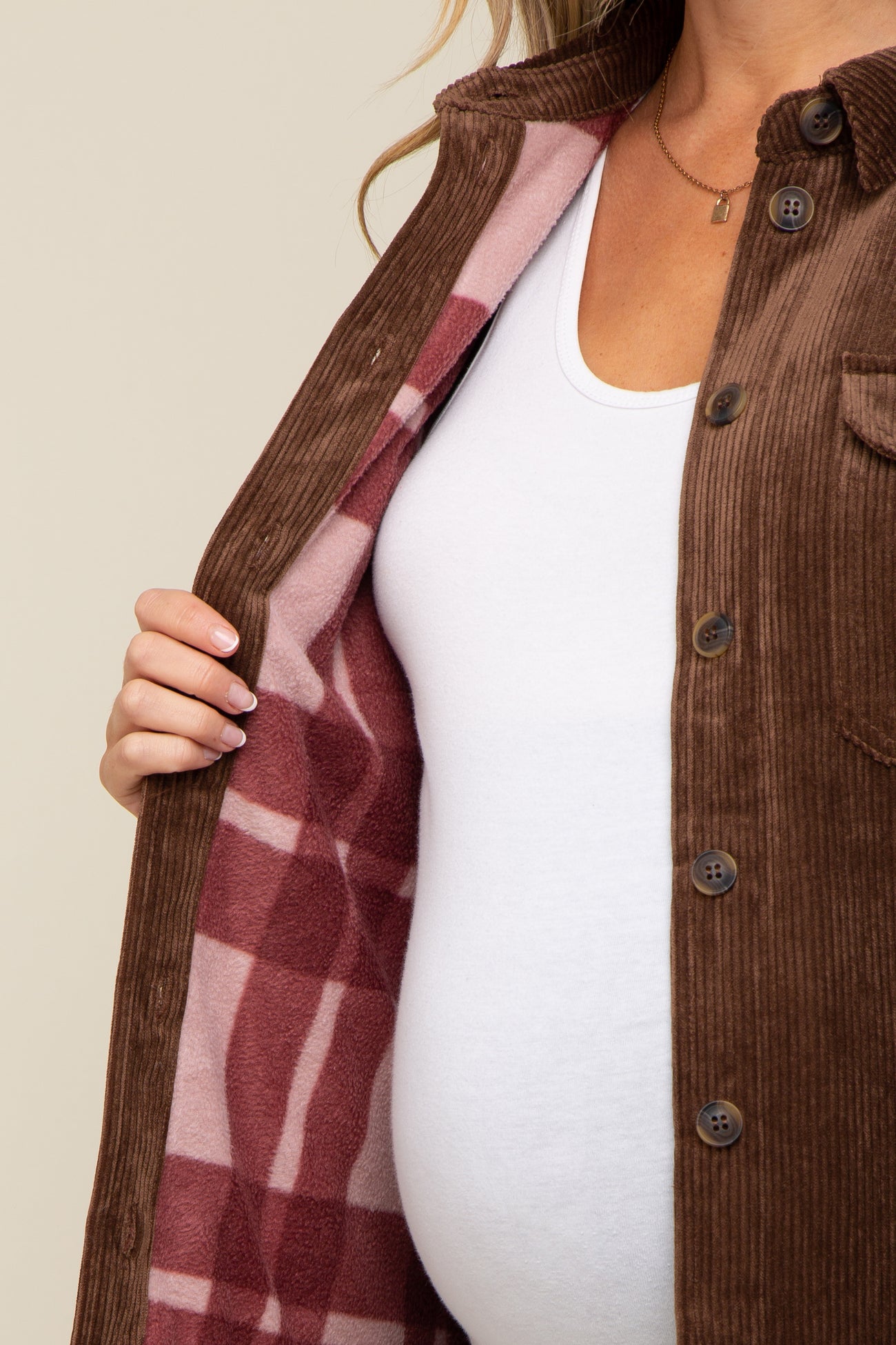 woman wearing brown corduroy shirt jacket with pink plaid fleece lining over a white maternity top