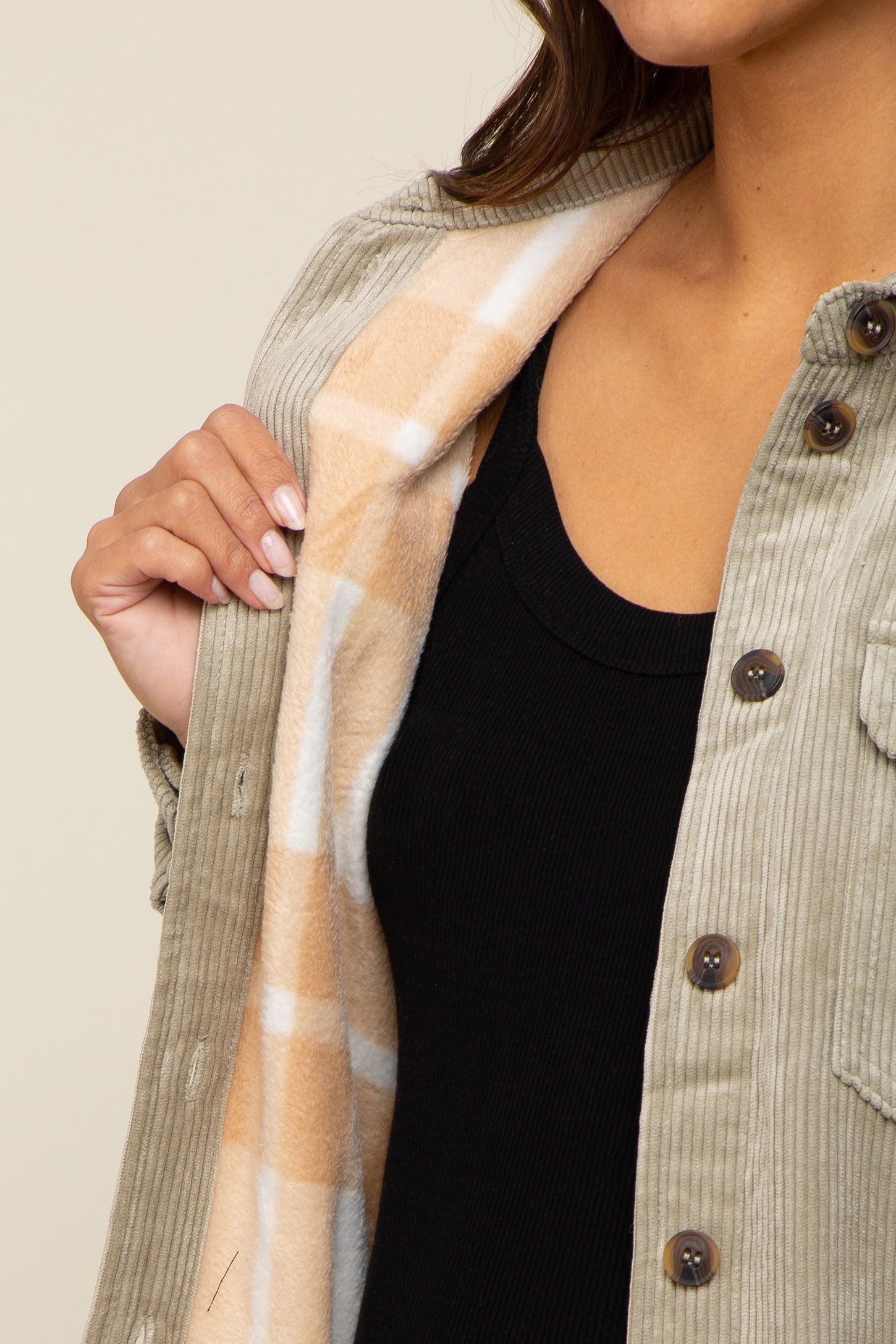 Close up of a woman wearing a sage green corduroy shirt jacket with a tan plaid fleece lining over a black top