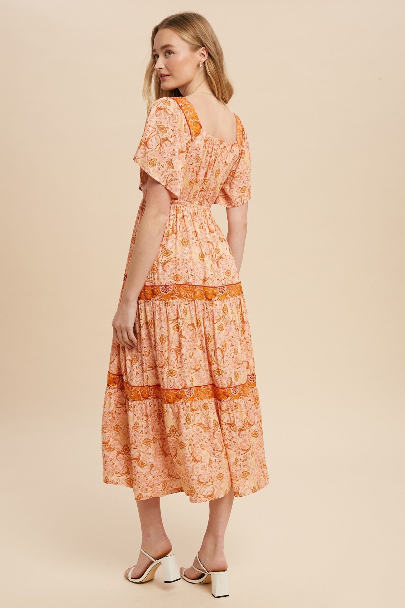 woman wearing a pink floral midi dress with short sleeves and a tiered skirt, showing the back view