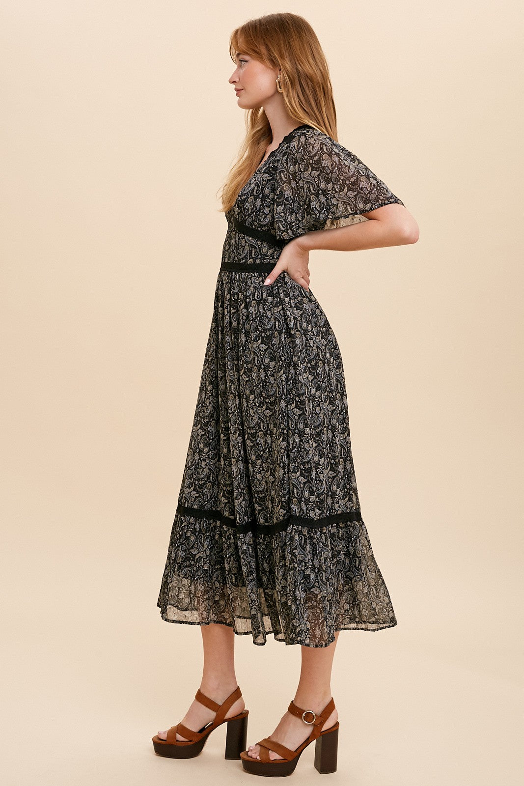 woman wearing a black floral mid-length dress with short sleeves and a tiered skirt, paired with brown heeled sandals