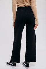 Back view of a person wearing black wide-leg knit trousers and black sneakers