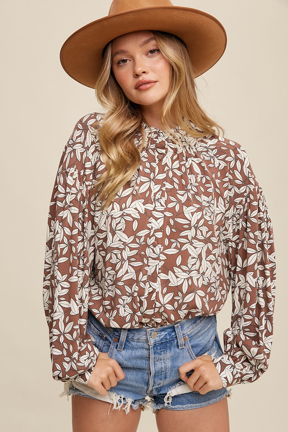 woman wearing brown floral print long sleeve blouse with denim shorts and a wide brim felt hat