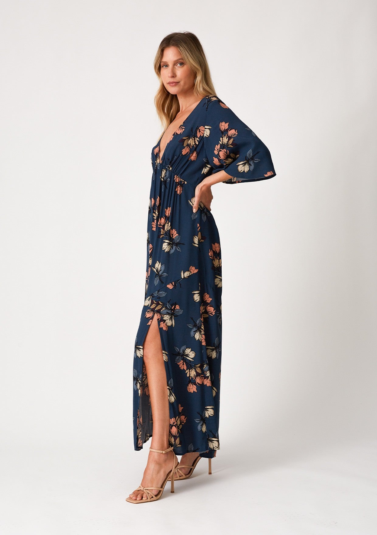 woman wearing a navy blue floral maxi dress with a leg slit and tan high heel sandals