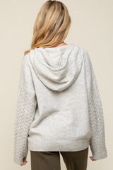 woman wearing a light gray maternity hoodie with a cable knit design on the sleeves and a hood