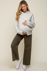 woman wearing a gray maternity hoodie with cable knit sleeves and olive green wide-leg pants, holding her baby bump