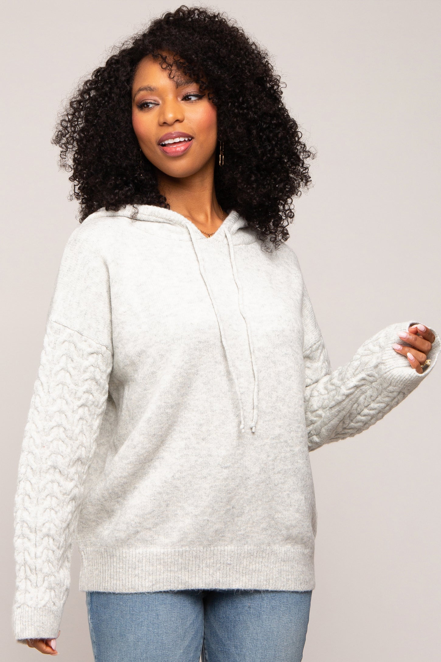 woman wearing a light gray oversized hoodie with cable knit sleeves and a drawstring hood