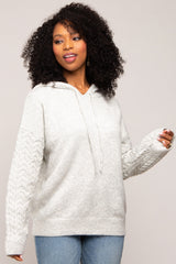 woman wearing a light gray oversized hoodie with cable knit sleeves and a drawstring hood