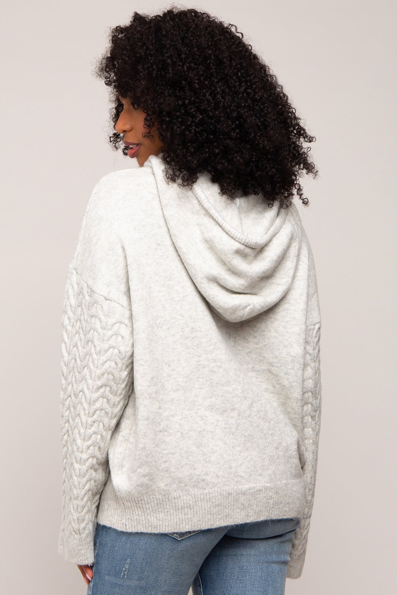 woman wearing a light grey hooded sweater with cable knit detailing and a relaxed fit, seen from the back