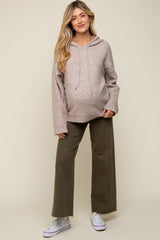 woman wearing a light pink maternity hoodie with cable knit sleeves and olive green wide-leg pants, showing her baby bump