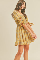 woman wearing a yellow plaid short dress with puff sleeves and tie details, standing sideways and smiling