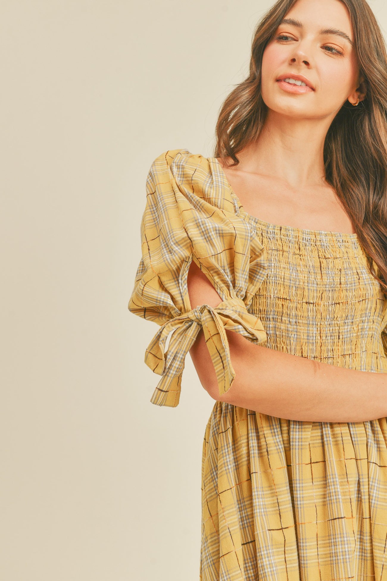 woman wearing a yellow smocked dress with plaid pattern and puff sleeves tied at the elbows