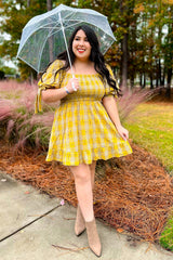 woman wearing a yellow plaid off-shoulder dress and holding a clear umbrella in an outdoor setting