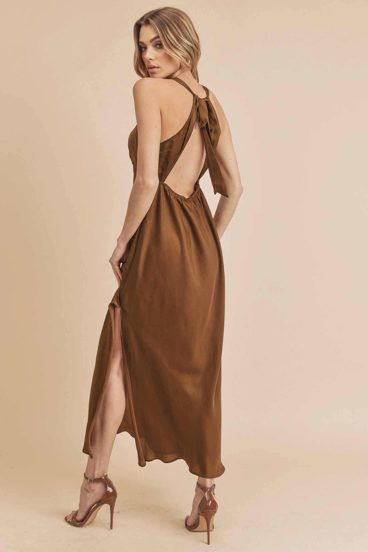 woman wearing a brown satin backless maxi dress with a side slit and high heels