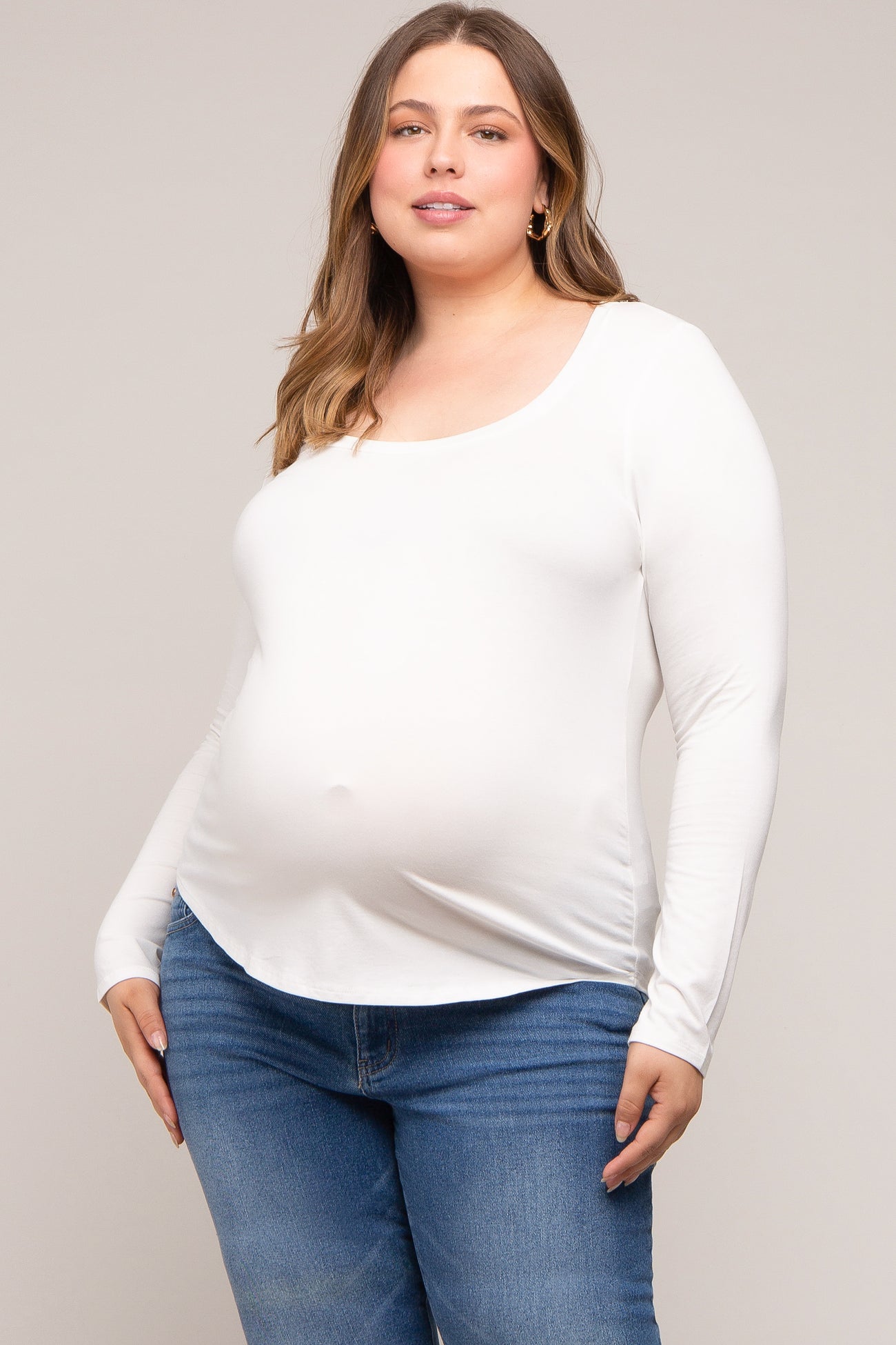 woman wearing a white long sleeve maternity top and showing her baby bump with blue jeans