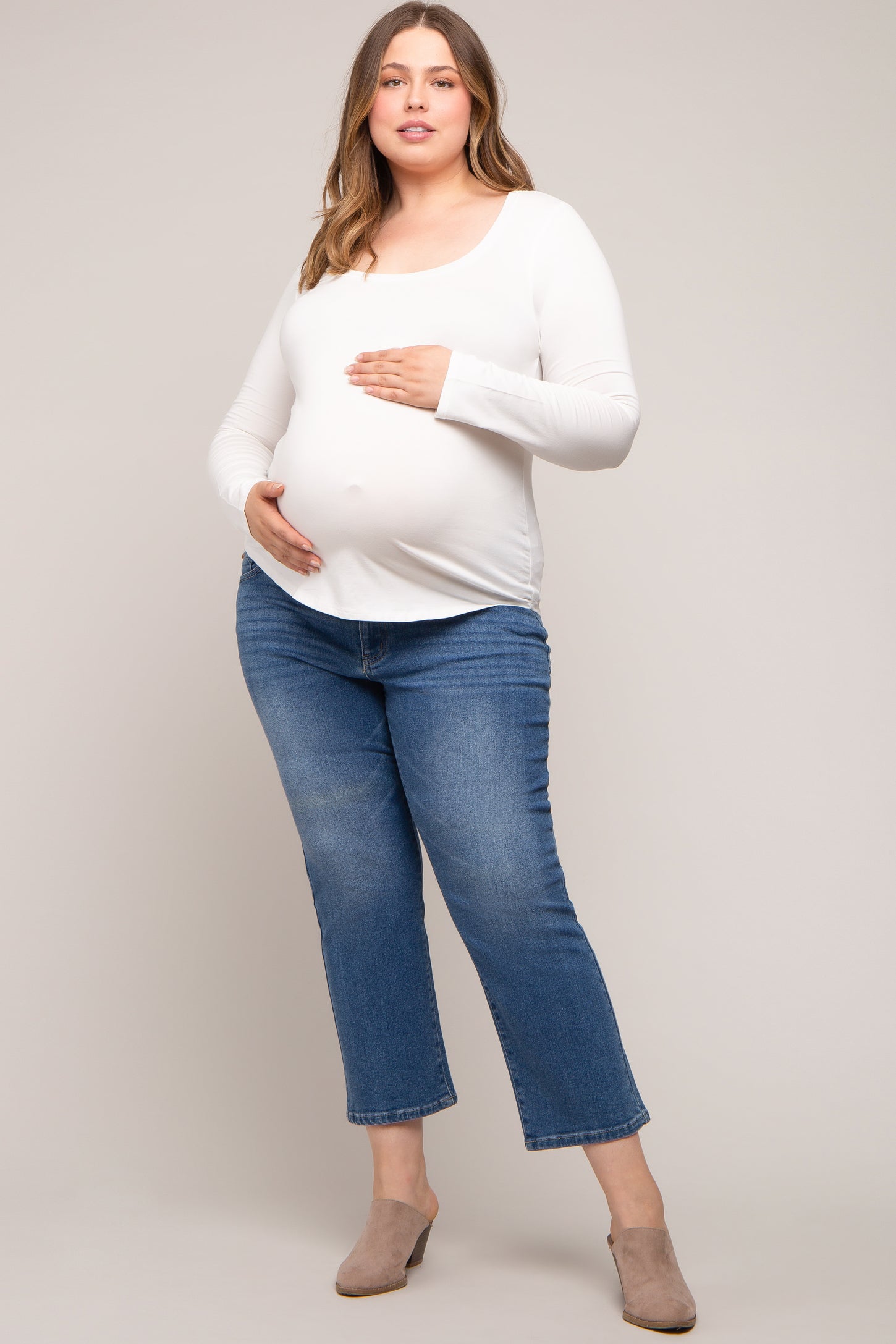 woman wearing a white long sleeve maternity top and blue cropped jeans, showing her baby bump