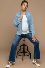 woman wearing a light blue denim button-up shirt over a white maternity top and distressed flared jeans, showing her baby bump