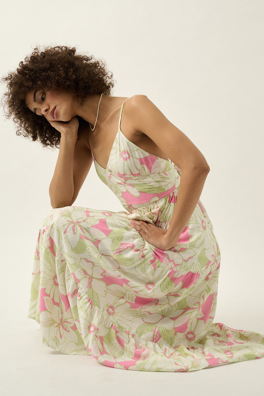 woman wearing a floral maxi dress with pink and green patterns, styled with spaghetti straps and a cinched waist