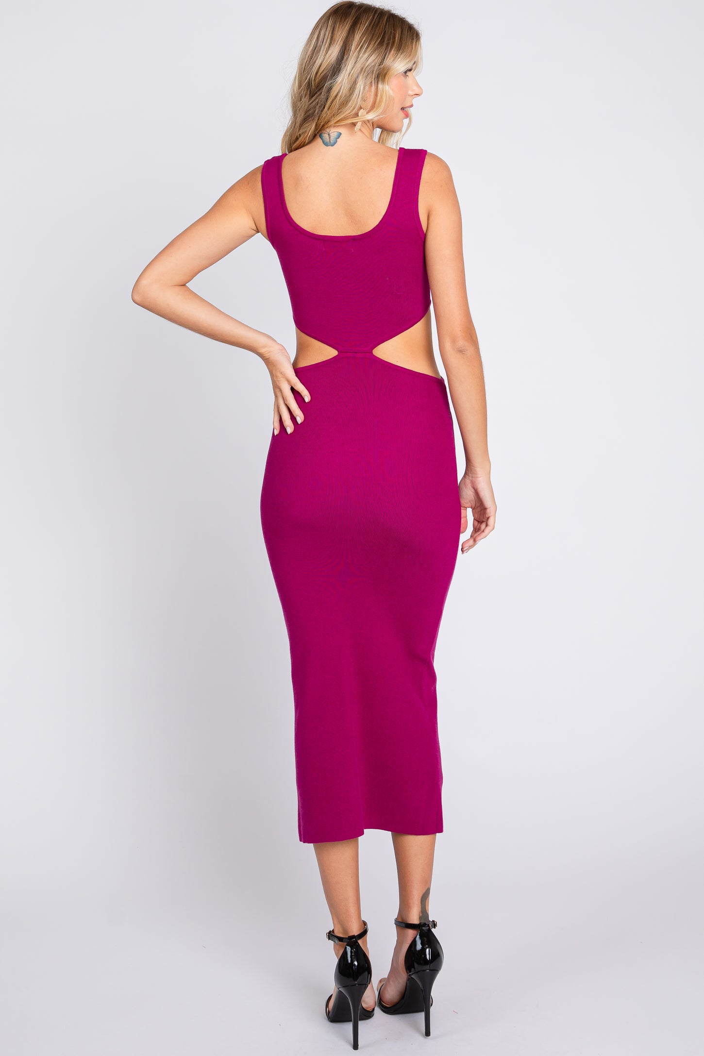 woman wearing a fuchsia midi dress with cut-out details and a scoop back, paired with black high heels