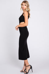 woman wearing a black fitted knit midi dress with a sleeveless design and side slit, paired with black heels