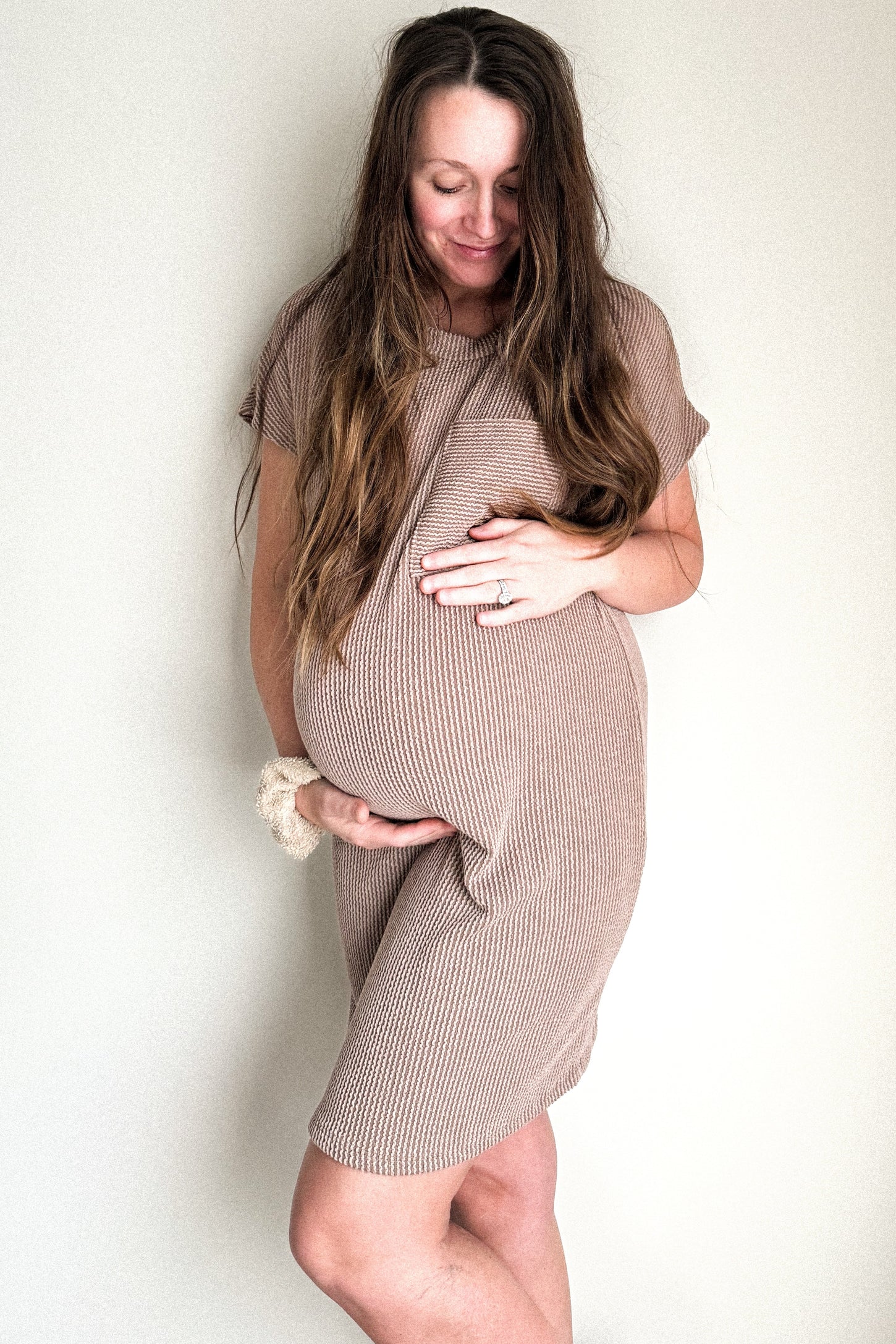 woman wearing a brown ribbed short sleeve maternity dress and holding her baby bump
