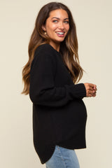woman wearing a black maternity sweater with textured knit and side slits, showing her baby bump