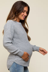 woman wearing a light gray maternity sweater with a textured pattern and a visible baby bump