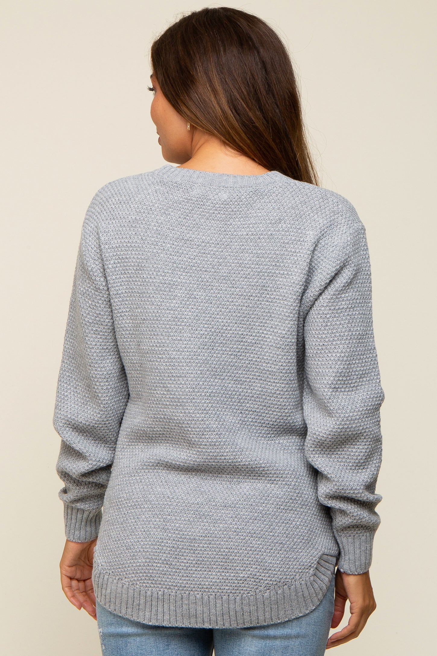 woman wearing a grey maternity sweater with a textured knit and longer back hem