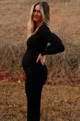 woman wearing a black long sleeve maternity dress showcasing her baby bump in a natural outdoor setting