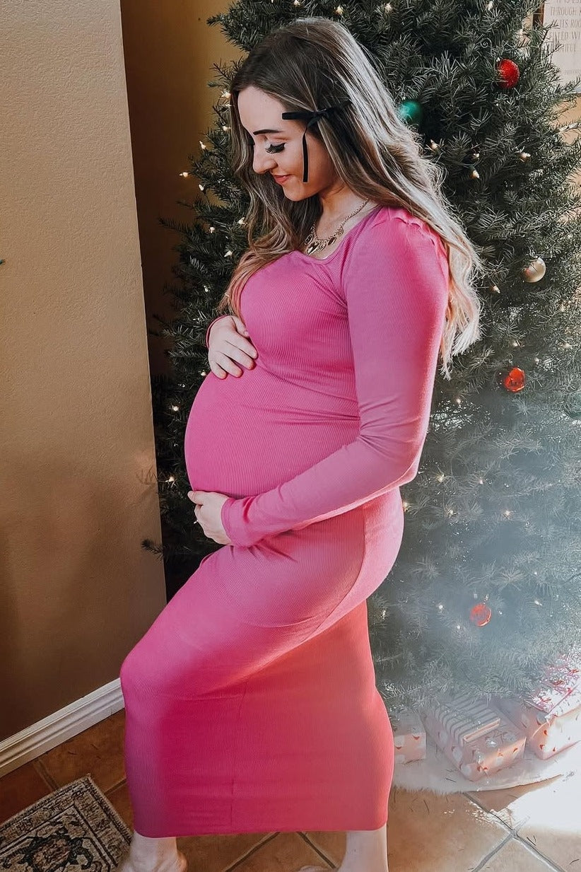 woman wearing a hot pink ribbed maternity dress showcasing her baby bump in front of a decorated Christmas tree