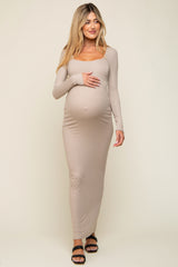 woman wearing a beige long sleeve maternity maxi dress and holding her baby bump